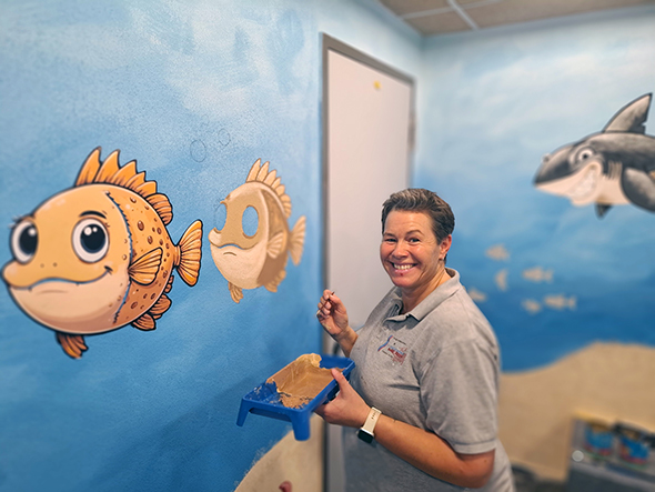 Ein Foto von Melanie Lewandowski von der Firma Sven Zylakowski Malermeister GmbH, die im neuen Wickelraum eine farbenfrohe, phantasievolle Unterwasserwelt geschaffen hat..